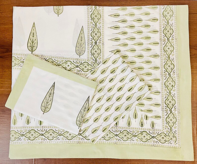 May include: A set of green and white cotton napkins with a leaf pattern. The napkins are folded and arranged on a green and white patterned fabric.
