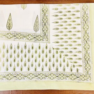 May include: A white cotton tablecloth with a green leaf pattern. The tablecloth has a border with a repeating design of green leaves and swirls.
