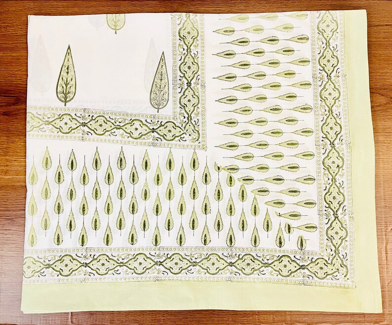 May include: A white cotton tablecloth with a green leaf pattern. The tablecloth has a border with a repeating design of green leaves and swirls.