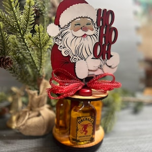 May include: Wooden Santa Claus figurine with a red hat and beard, holding a sign that says "Ho Ho Oh". The figurine is holding a bottle of Fireball Cinnamon Whisky. The figurine is on a wooden stand with a red ribbon.
