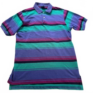 May include: A short-sleeved polo shirt featuring a horizontal striped pattern in shades of purple, teal, and dark navy blue. The shirt has a classic collar, a two-button placket with white buttons, and a straight hemline with small side vents.