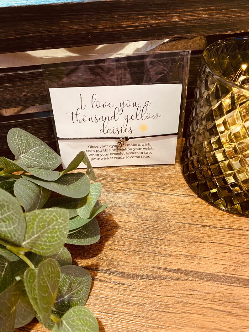 May include: A black bracelet with a small gold daisy charm. The bracelet has a message that reads "I love you a thousand yellow daisies. Close your eyes, make a wish, then put this bracelet on your wrist. When your bracelet breaks in two, your wish is ready to come true."