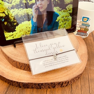 May include: A white card with the text "I love you a thousand yellow daisies" and a black string bracelet with a silver daisy charm. The card also includes instructions for making a wish with the bracelet.