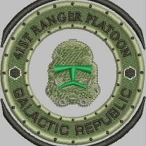 May include: A green and black embroidered patch with a circular design. The center of the patch features a white and green stylized image of a helmet. The text "41st Ranger Platoon Galactic Republic" is written in a circle around the helmet.