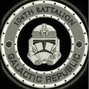 May include: Embroidered patch featuring a detailed design. The patch has a circular shape with the text "104th Battalion" and "Galactic Republic" in a ring around a central image of a helmet. The helmet is white with black accents, set against a gray background.
