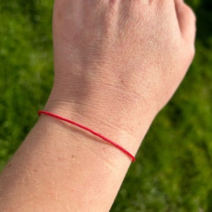 May include: A red string bracelet worn on a person's wrist.