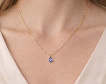 May include: A delicate gold-tone necklace featuring a small, round pendant with a blue eye design. The pendant has a blue center with a black outline and a gold-tone border. The necklace is a simple chain, suitable for everyday wear.