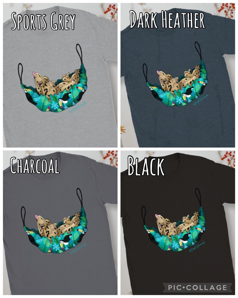 May include: Four t-shirts in sports grey, dark heather, charcoal, and black. Each shirt features a graphic of a gecko relaxing in a hammock made of tropical leaves and toucans. The text "SPORTS GREY", "DARK HEATHER", "CHARCOAL", and "BLACK" are displayed above each shirt.