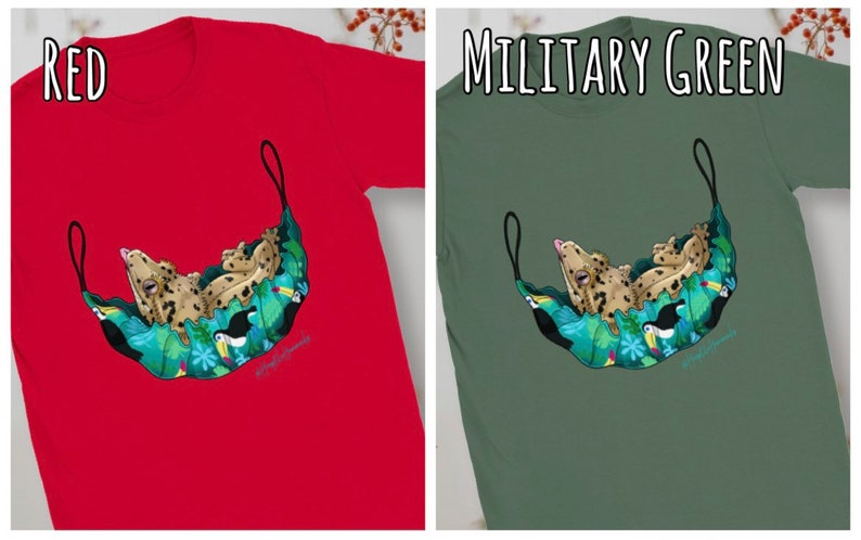 May include: Red t-shirt featuring a whimsical illustration of a leopard-like creature lounging in a hammock adorned with tropical flowers and toucans. The design is set against a solid red background. The text "RED" is at the top.