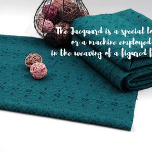May include: Teal blue fabric with a delicate, intricate lace pattern. The fabric is folded and stacked, showcasing the texture and detail of the lace. The text "The Jacquard is a special loom, or a machine employed in the weaving of a figured fabric." is visible in the image.