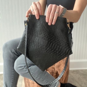 May include: A black leather crossbody bag with a snakeskin pattern. The bag has a long strap and a flap closure.