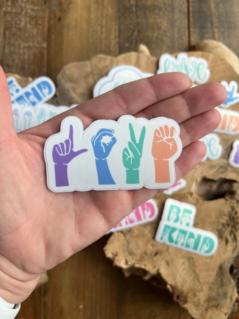 Puede incluir: Una pegatina con la palabra "LOVE" escrita en lenguaje de se&ntilde;as. Cada letra es de un color diferente del arco&iacute;ris.