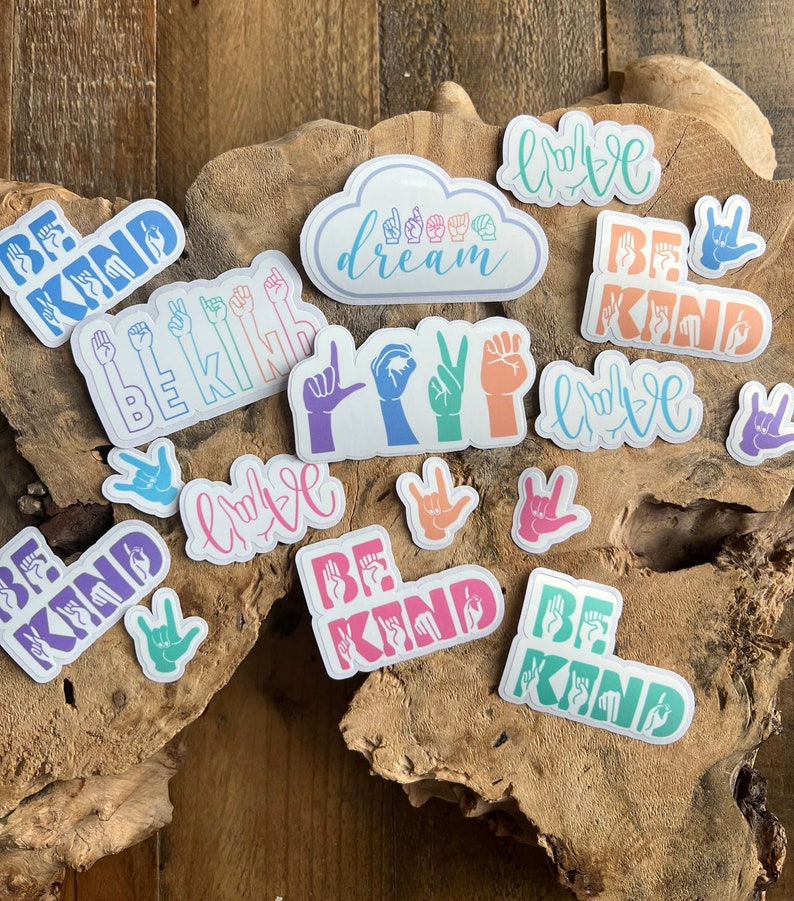 Puede incluir: Un conjunto de pegatinas coloridas que presentan el lenguaje de se&ntilde;as para "ser amable" y "amor" en una variedad de colores y estilos. Las pegatinas tambi&eacute;n incluyen las palabras "sue&ntilde;o" y "ser amable" en forma de nube.