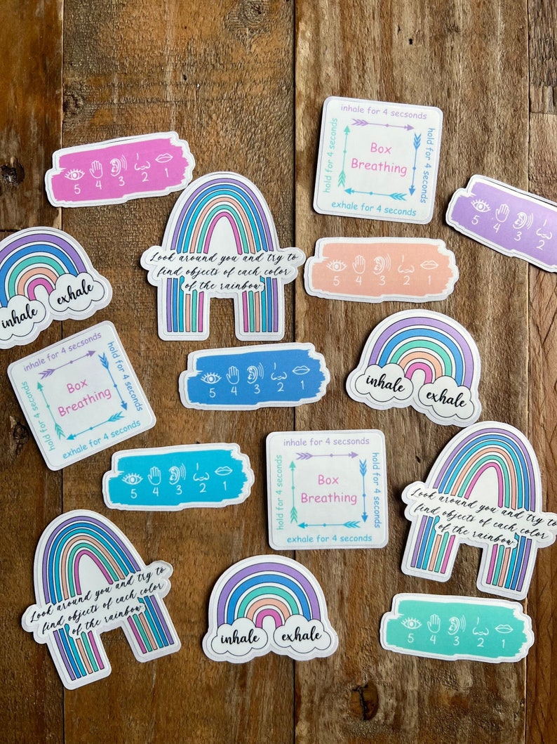 May include: A set of colorful rainbow stickers with the words "inhale" and "exhale" on them. The stickers also include instructions for box breathing and a hand sign guide for counting breaths.