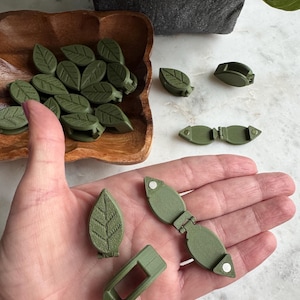 May include: A set of green leaf-shaped plant clips. The clips are made of plastic and have a spring mechanism to hold them in place. The clips are designed to look like leaves and are perfect for holding vines or other plants in place.