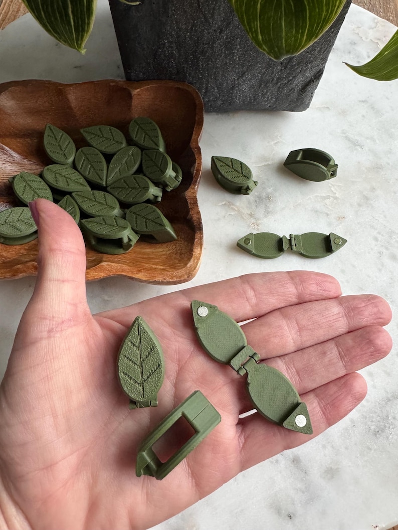 May include: A set of green leaf-shaped plant clips. The clips are made of plastic and have a spring mechanism to hold them in place. The clips are designed to look like leaves and are perfect for holding vines or other plants in place.