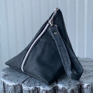 May include: A black triangular clutch bag with a snakeskin pattern and a silver zipper. The bag has a black strap with a silver buckle.