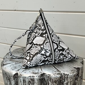 May include: A white and black snakeskin-patterned triangular handbag with a zipper closure and a top handle.