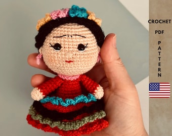 May include: Crochet pattern for a Frida Kahlo doll. The doll is wearing a red dress with black, green, and blue trim. The doll has black hair and a flower crown.