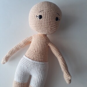 May include: A crocheted doll with a beige body and white shorts. The doll has black eyes and a simple embroidered face.