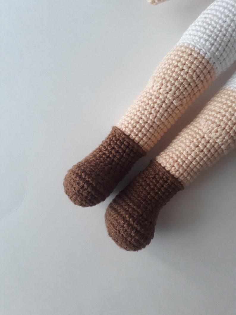 May include: Close-up of a pair of brown crocheted doll shoes. The shoes are made with a brown yarn and have a rounded toe.