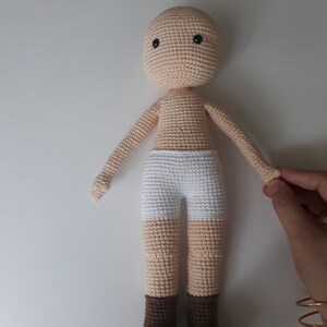 May include: A crocheted doll with a beige body, white underwear, and brown boots. The doll has black eyes and a simple face.