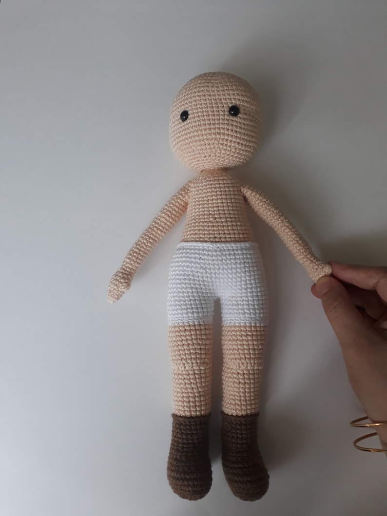 May include: A crocheted doll with a beige body, white underwear, and brown boots. The doll has black eyes and a simple face.