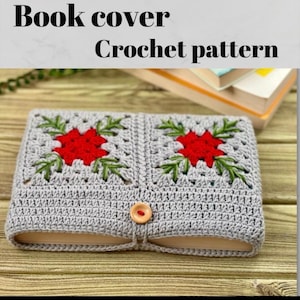 May include: A light grey crocheted book cover with a red flower and green leaf design. It has a button closure and the text "Book cover Crochet pattern". The book cover is displayed on a wooden surface.