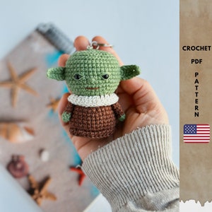 Può includere: Schema di uncinetto PDF per un amigurumi Yoda verde con abiti marroni. Lo schema è disponibile in inglese e include istruzioni per realizzare un portachiavi.