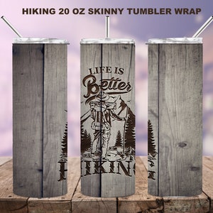 May include: A 20 oz skinny tumbler wrap with a wood grain design. The tumbler features the text "Life is Better Hiking" with an illustration of a hiker. The tumbler includes a silver lid and straw.