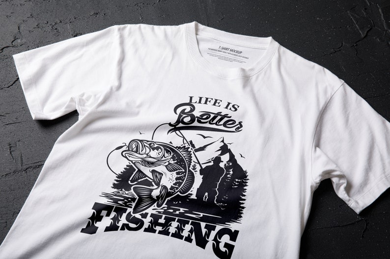 K&ouml;nnte beinhalten: Wei&szlig;es T-Shirt mit einem schwarzen Grafikdesign eines Fisches, der aus dem Wasser springt, mit dem Text "Life is Better Fishing".