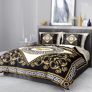 Op de afbeelding: Zwart en gouden beddengoed met een wit middenstuk met een gouden Grieks sleutelmotief. Het beddengoed ligt op een bed met twee bijpassende kussens.