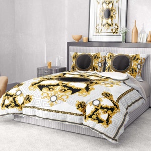 Op de afbeelding: Wit en gouden dekbedovertrek met een zwart en gouden geometrisch patroon. Het dekbedovertrek heeft een grote, sierlijke cirkel in het midden en kleinere cirkels in het hele ontwerp. Het dekbedovertrek ligt op een bed met twee bijpassende kussenslopen.