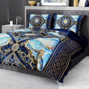 Op de afbeelding: Blauw en gouden beddengoed met een geometrisch patroon. De dekbedovertrek heeft een marmerachtig ontwerp met gouden accenten. De kussenslopen hebben een vergelijkbaar patroon met een cirkelvormig ontwerp in het midden.