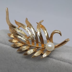 May include: A gold-tone brooch in the shape of a leaf with a single faux pearl accent.