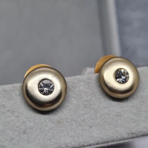 May include: A pair of gold-toned stud earrings with a clear rhinestone in the center of each earring.
