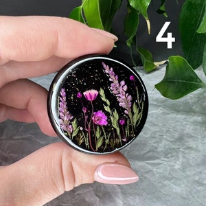 Pode incluir: Um objeto redondo de resina preta com um design floral. O design apresenta flores roxas e rosas, folhas verdes e flocos dourados. O n&uacute;mero "4" &eacute; vis&iacute;vel em branco no fundo.