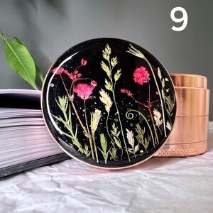 Pode incluir: Uma base redonda de resina preta com flores secas rosa, verdes e brancas embutidas. A base tem uma borda cor de cobre e est&aacute; ao lado de um moedor cor de cobre.