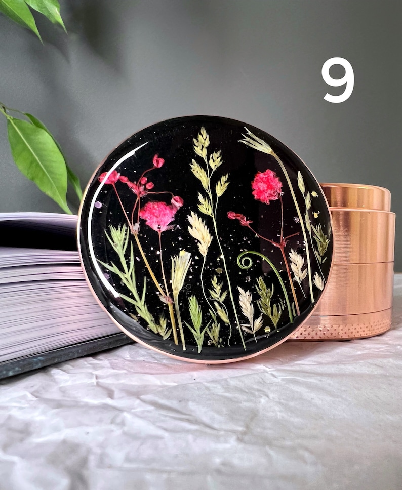 Pode incluir: Uma base redonda de resina preta com flores secas rosa, verdes e brancas embutidas. A base tem uma borda cor de cobre e est&aacute; ao lado de um moedor cor de cobre.