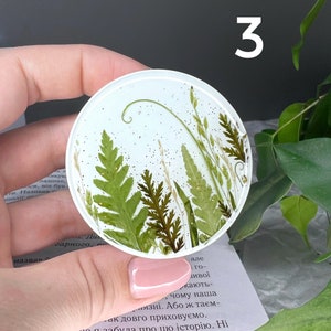 Pode incluir: Uma base de resina redonda e transparente com samambaias e gram&iacute;neas secas embutidas. A base tem um fundo azul claro com detalhes de glitter e o n&uacute;mero "3" em branco. Um item de decora&ccedil;&atilde;o para casa &uacute;nico.