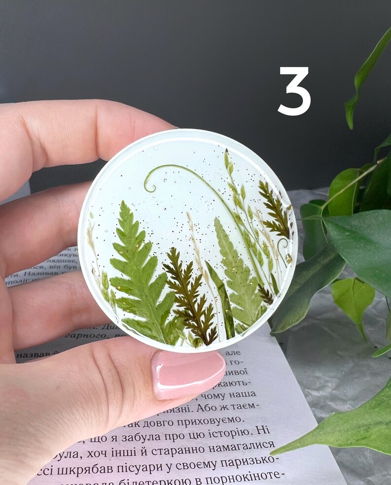 Pode incluir: Uma base de resina redonda e transparente com samambaias e gram&iacute;neas secas embutidas. A base tem um fundo azul claro com detalhes de glitter e o n&uacute;mero "3" em branco. Um item de decora&ccedil;&atilde;o para casa &uacute;nico.