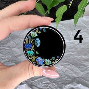 K&ouml;nnte beinhalten: Ein schwarzer Handy-Griff mit wei&szlig;em Rand und einem Blumendesign mit blauen und gr&uuml;nen Blumen. Die Zahl 4 ist im Hintergrund sichtbar.