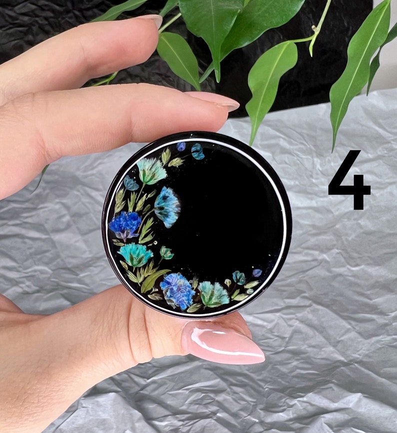 K&ouml;nnte beinhalten: Ein schwarzer Handy-Griff mit wei&szlig;em Rand und einem Blumendesign mit blauen und gr&uuml;nen Blumen. Die Zahl 4 ist im Hintergrund sichtbar.