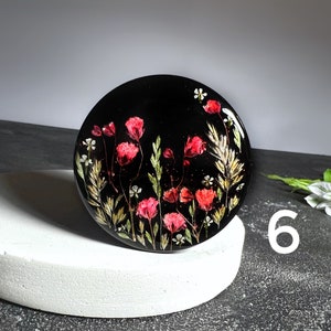 K&ouml;nnte beinhalten: Ein runder schwarzer Untersetzer mit einem Blumendesign aus roten und wei&szlig;en gepressten Blumen. Der Untersetzer befindet sich auf einer wei&szlig;en Oberfl&auml;che.