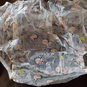 May include: A white plastic diaper cover with a colorful print of babies and stars. The cover has elastic around the legs and waist.