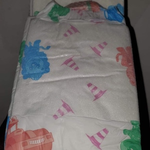 May include: A stack of three white disposable diapers with colorful cartoon animal and construction vehicle designs. The diapers have pink and white striped cones printed on them.