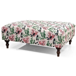 May include: A white ottoman with a floral print featuring hummingbirds and cacti. The ottoman has four dark brown wooden legs.