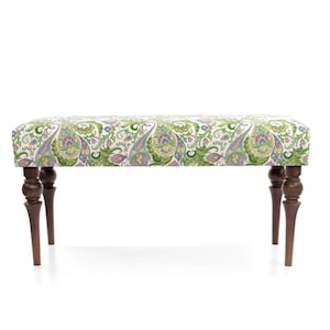 May include: A decorative bench with a paisley pattern in green, pink, and blue on a white background. The bench has four dark brown, turned legs. This upholstered bench is suitable for a living room or bedroom.