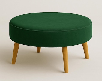 May include: A round, emerald green velvet ottoman with a light wood base. The ottoman has a low profile and is supported by four angled, tapered legs. The seat cushion is a solid, deep green color.