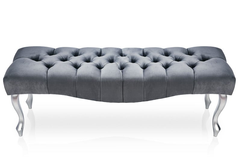 May include: A gray tufted bench with silver legs. The bench has a curved shape and a button tufted design.